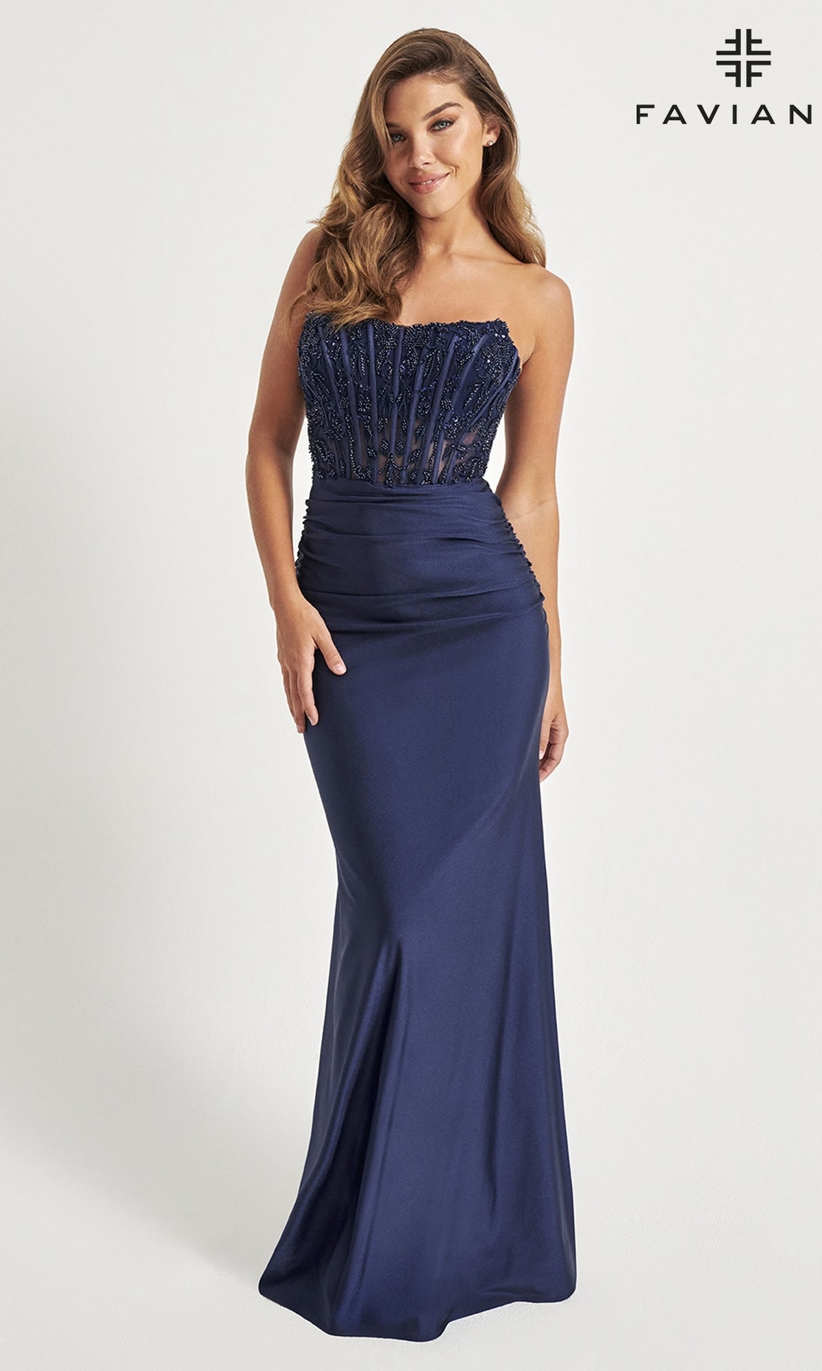 A woman models the Corset Faviana Strapless Long Formal Dress 11081 in navy blue, with a fitted beaded bodice and smooth skirt, standing against a white background. The